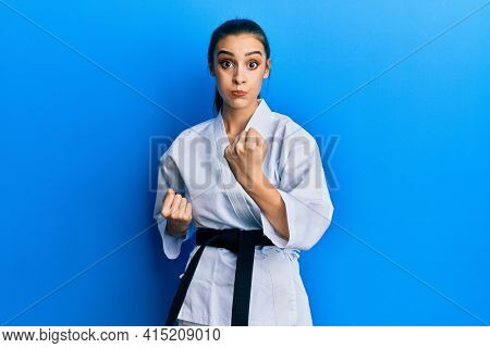 Beautiful brunette young woman wearing karate fighter uniform with black belt doing attack pose puffing cheeks with funny face. mouth inflated with air, catching air. 