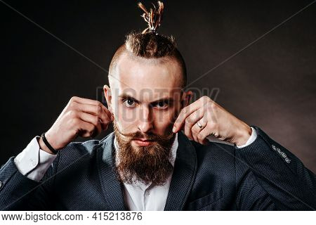 Portrait Of A Young Bearded Hipster Man Who Dangles A Long Mustache Against A Dark Background In The