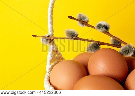 Yellow Background With Straw Handmade Basket Full Of Eggs And Pussy Willow Twig. Copy Space. Empty T