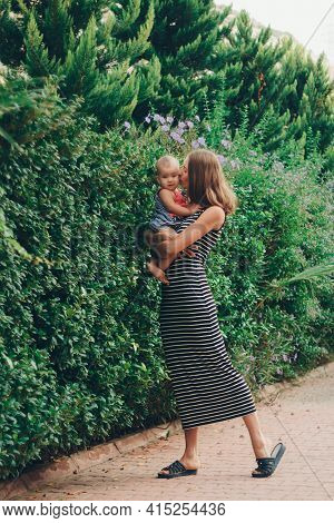 A Small Child Sits On The Mothers Hands. Momys Daughter Is On Vacation. Tropical Leaves. Travel To H