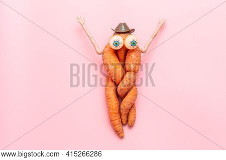 Funny Ugly Twisted Carrot On A Pink Background. Carrots With Hands, Eyes And A Hat. Vegetable Toy