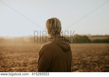 Blonde man in stretchy hoodie watching sunset in the countryside