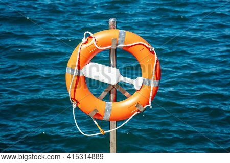 Lifebuoy Orange On Vertical Iron Against Blue Sea Background.