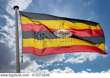 Uganda Flag, Republic Of Uganda National Symbol On A Flagpole Waving Against Blue Cloudy Sky