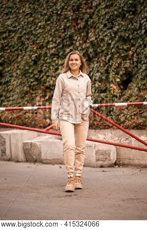 A Pretty Blonde Young Woman Is Walking Down The Street, She Is Wearing Jeans And A Beige Shirt. Beau
