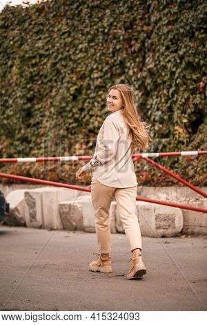 A Pretty Blonde Young Woman Is Walking Down The Street, She Is Wearing Jeans And A Beige Shirt. Beau