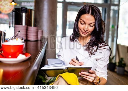 Indian Reading Notes In Notepad While Sitting Near Table Bar And Drinling Cup Of Tea