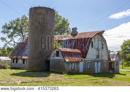 An Abandoned Old Farm House With A Tall Brick Silo And A Big Barn With Rusted Tin Ceiling. This Very