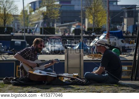 Bristol/uk 04/17/2010: Two Men Sit Crosslegged On The Floor, Drinking Beer And Playing Classical Gui