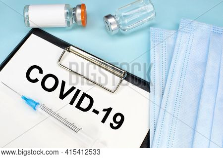 The Inscription Cоvid-19 On A Stationery Tablet That Lies On A Blue Background Near A Medical Face M