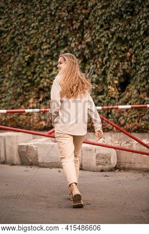 A Pretty Blonde Young Woman Is Walking Down The Street, She Is Wearing Jeans And A Beige Shirt. Beau