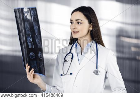 Professional Young Woman-doctor Is Looking At Her Patients Roentgenogram. Physician At Work In A Cli