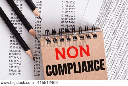 The Words Non Compliance Is Written On The Brown Notebook. Nearby Pencils