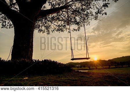 Silhouette Of A Wooden Swing Under The Tree. Lonely And Relaxing Golden Ligth On Sunset On Summer Ho