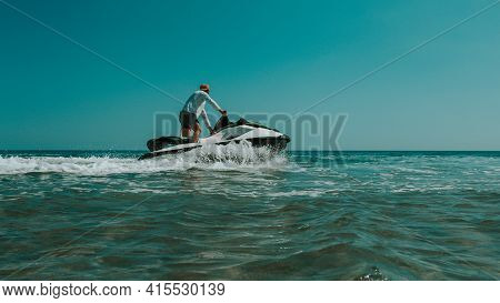 A Man On A Jet Ski Ride, The Sea And The Ocean In Clothes, Hot Weather With The Rays Of The Bright S