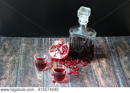 Homemade Pomegranate Liqueur In A Bottle And Two Glasses And A Broken Fruit With A Scattering Of See