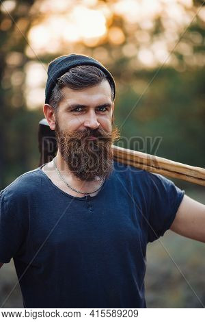 Brutal Bearded Man Lumberjack With A Long Beard And Mustache In A T-shirt And A Warm Hat With An Ax