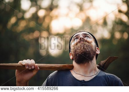 A Bearded Man In A Dark Sleeveless T-shirt With A Large Mustache And Gray Hair Holds An Iron Ax On H