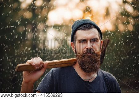 Brutal Lumberjack In A Dark Sleeveless T-shirt With A Large Mustache And Gray Hair Holds An Iron Ax