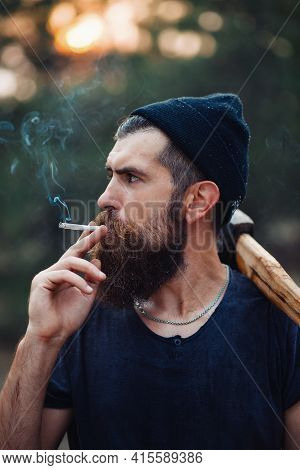 Old Bearded Stylish Man In A Dark Sleeveless T-shirt And In A Warm Hat With A Large Mustache And Gra