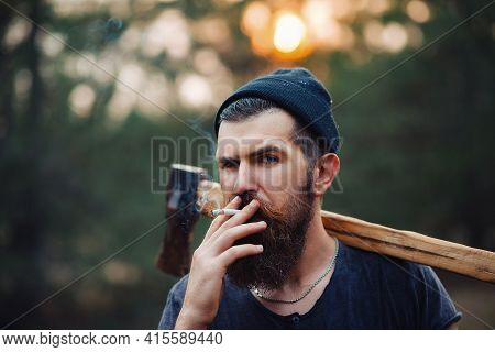 Adult Bearded Stylish Man In A Dark Sleeveless T-shirt And In A Warm Hat With A Large Mustache And G