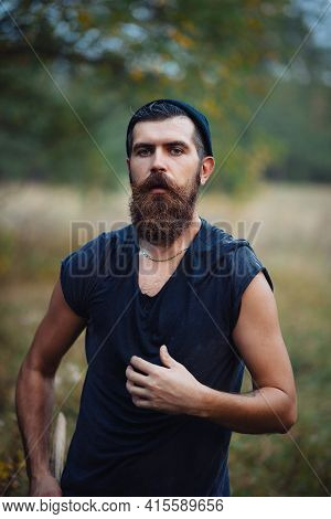 Bearded Man With A Thick Beard And A Large Mustache In A Dark Sleeveless T-shirt And A Warm Hat With