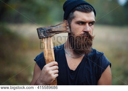 A Bearded Man With A Large Mustache In A Dark Sleeveless T-shirt And A Warm Hat With Gray Hair Holds
