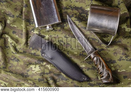 Knife, Scabbard, Metal Flask And Mug On Camouflage Fabric. Large Knife With Wooden Handle, Black Lea