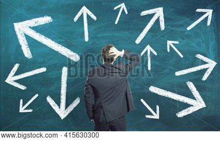 Businessman Standing Confused In Front Of A Green Background With White Arrows, Choice And Path Dile