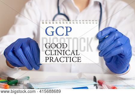 Gcp Card In Hands Of Medical Doctor. Doctor's Hands In Blue Gloves Holding A Sheet Of Paper With Tex
