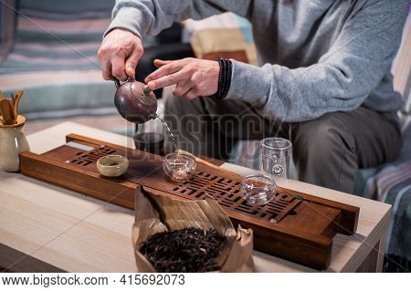 The Master Of Tea Ceremonies Pours Amber Tea In A Thin Stream Into Tasting Cups. Close-up With A Blu