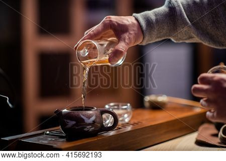 Close-up Of A Traditional Oriental Tea Ritual. A Man Pours Black Ripe Tea From A Flask Into A Tastin