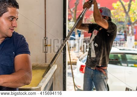 Middle-aged Man Wearing A Cap Is Moving The Corn For Proper Cooking While Another Man Watches As He 