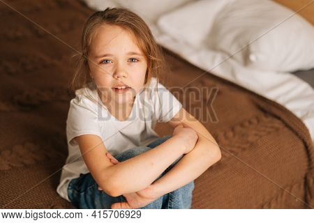 Top Close-up View Of Distraught Beautiful Little Girl With Wet Eyes From Tears Sits On Bed In Bedroo