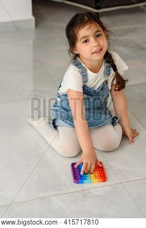 Young Little Girl Sitting On The Floor At Home Playing Poppit-new Fidget Toy, Popular With Kids, Hel