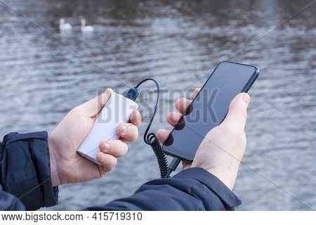 A Man Charges A Smartphone With A Power Bank. The Phone In Hand Is Being Charged With A Portable Cha