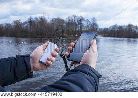 A Man Charges A Smartphone With A Power Bank. The Phone In Hand Is Being Charged With A Portable Cha