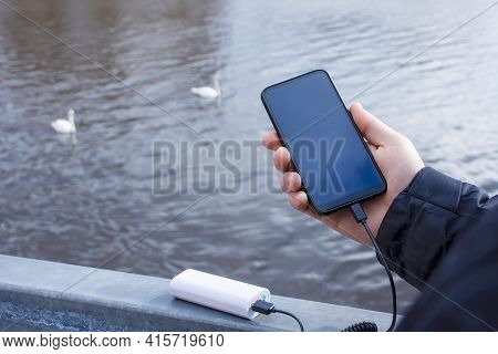 A Man Charges A Smartphone With A Power Bank. The Phone In Hand Is Being Charged With A Portable Cha
