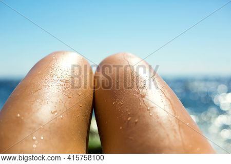 Smooth Tanned Female Legs In The Spray Of Water On The Beach Against The Background Of The Sea. Tann