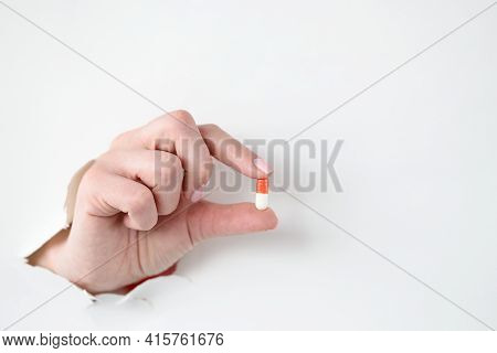Female Hand Holds Medical Pill Through Hole Through White Paper