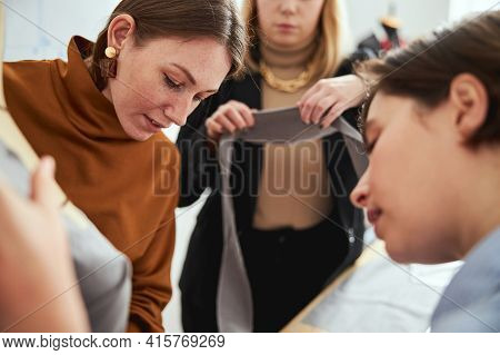 Couturiere Bringing Long Grey Fabric Snip To Two Females