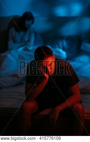 Unhappy Couple. Night Problem. Male Dysfunction. Depressed Overthinking Man Sitting On Bed On Distan