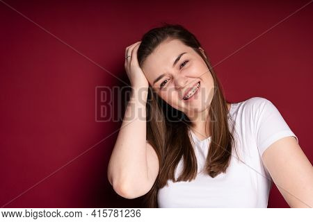 Smiling Girl With Braces Tilting Her Head Touches Her And Looks At The Camera While Standing On A Br