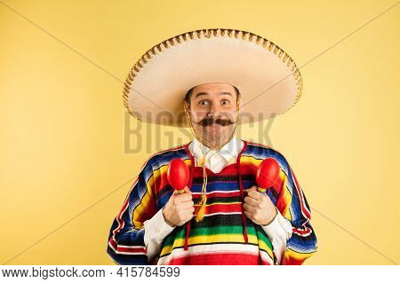 Happy Man In Sombrero And Bright Poncho Isolated Over Yellow Background