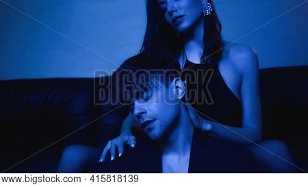 Brunette Woman Sitting On Couch And Embracing Man In Blazer On Blue.