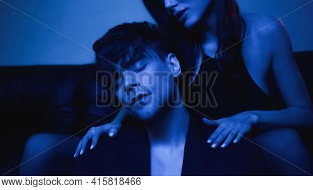 Brunette Woman Sitting On Couch And Hugging Man In Blazer On Blue.