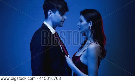 Side View Of Seductive Woman Pulling Tie Of Man In Blazer On Blue.
