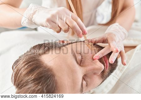 Concept Of Cosmetology And Facial. A Woman Beautician Makes Face And Beard Modeling For A Man Waxing