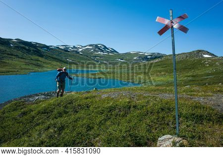Hiking in Swedish Lapland. Man traveler trekking alone with view of mountain lake Allagasjavri in northern Sweden. Arctic nature of Scandinavia in warm summer sunny day with blue sky