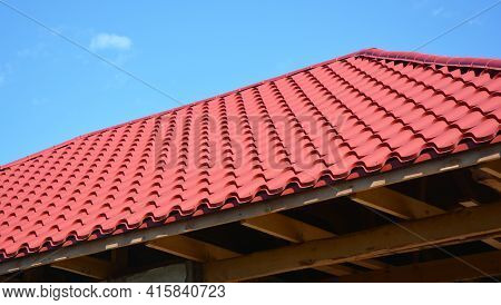 A Close-up Of An Unfinished Metal Roof With Red Metal Roofing Tiles, Wood Ceiling Joists, Eaves, And